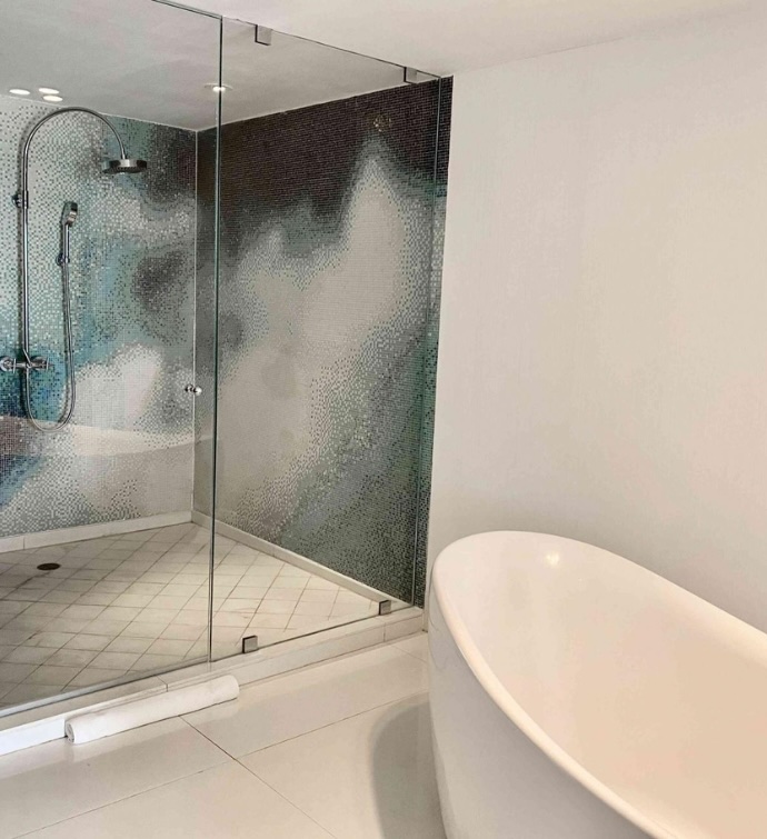 Corner of large white bathtub and a walk-in shower with an ombre blue wall