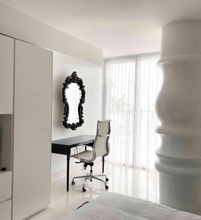 Habitación blanca con silla de escritorio blanca, escritorio negro y espejo con marco negro en la pared