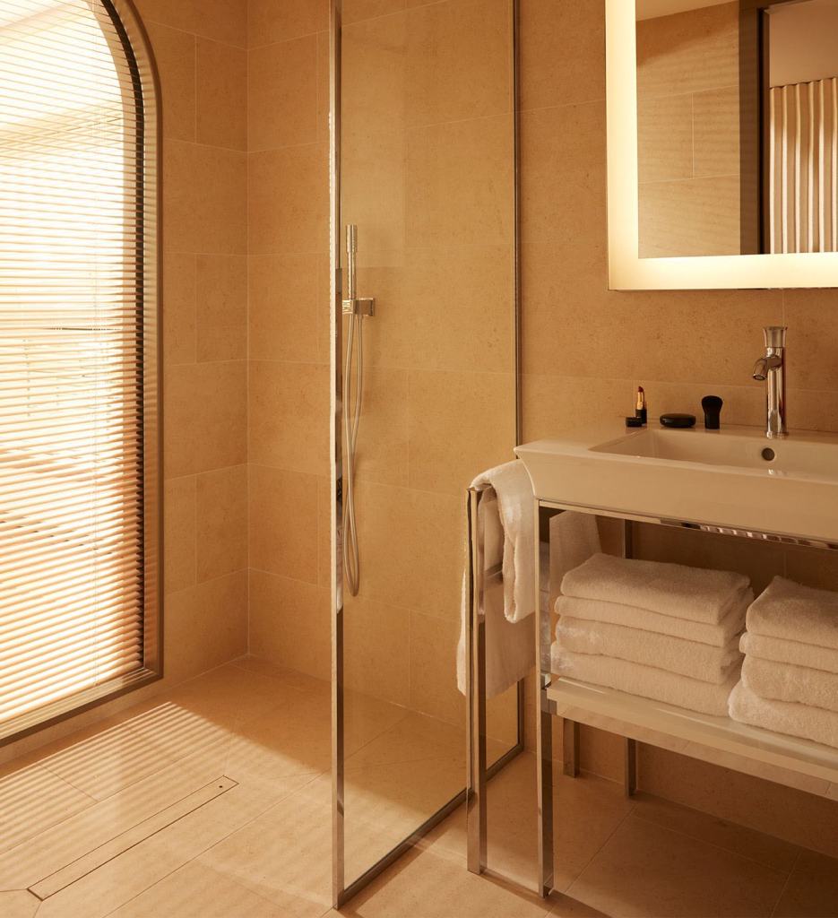 Salle de bain avec miroir éclairé, douche et lavabo avec des serviettes sous la vasque