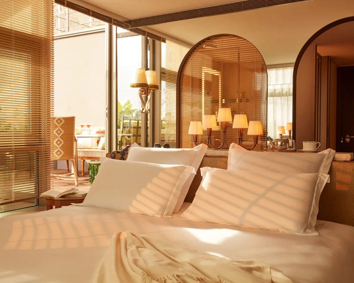 Premier terrace king room at Mondrian Bordeaux Les Carmes. Bed is shown with crisp white sheets and golden sunshine peering through.