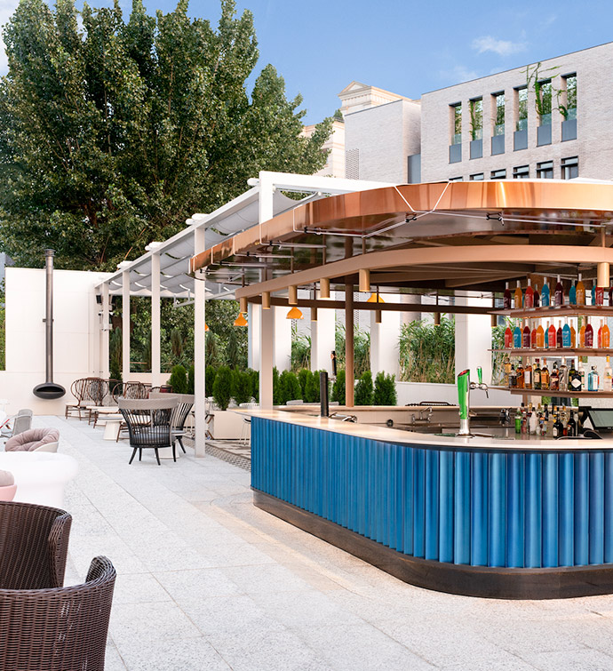 Outdoor, curved bar with a royal blue fluted base and copper-colored covering, and patio seating in the distance