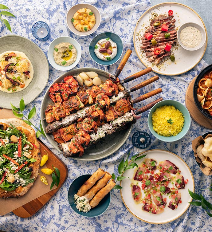 A spread of Mediterranean food captured from overhead, including grilled kebabs, hummus, rice, pita, flatbread, couscous and more