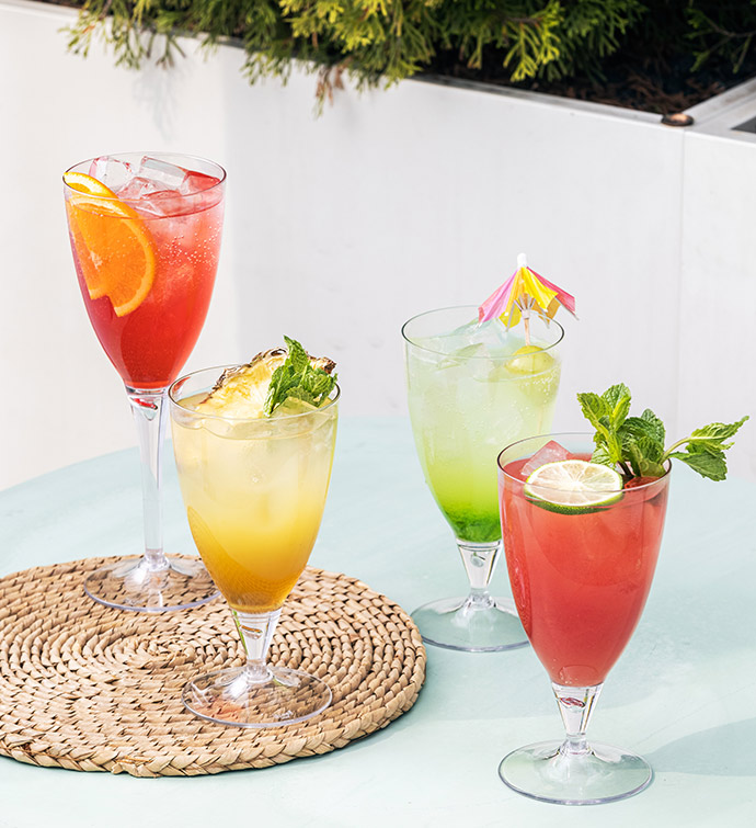 a range of red, green and orange cocktails garnished with oranges, mint, lime, pineapple and umbrella