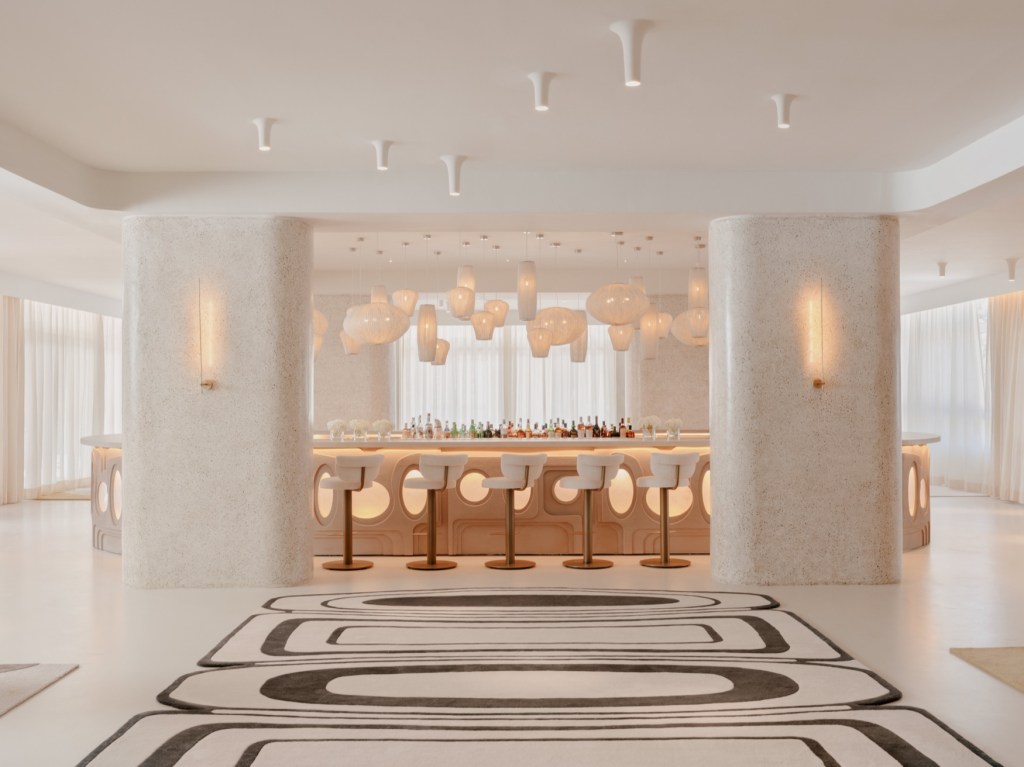 Beautiful modern white bar with white pendant lights, black and white geometric rug, and barstools.