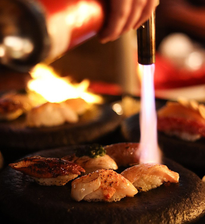 Piece of sushi being lightly charred with a blowtorch 