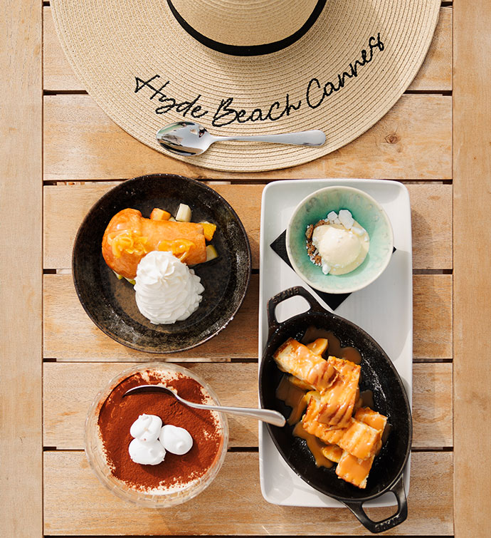 A selection of four desserts photographed from above alongside a sunhat with the brim embroidered with Hyde Beach Cannes in script