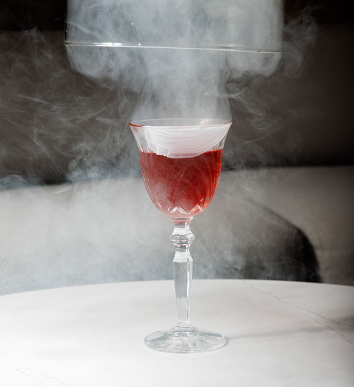 Un cocktail rouge photographié dans un nuage de fumée