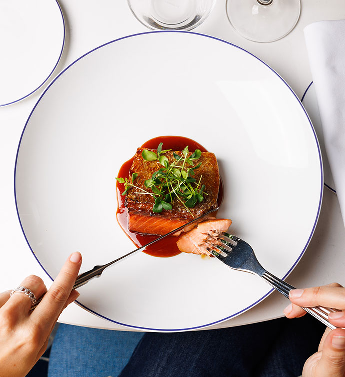 Des mains coupant un filet de poisson à l'aide d'une fourchette et d'un couteau