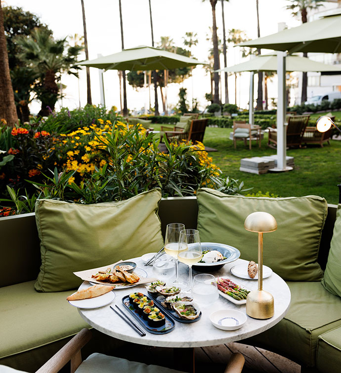 Outdoor dining patio with light green cushions and umbrellas, and a table set with an array of dishes from Mr Nakamoto