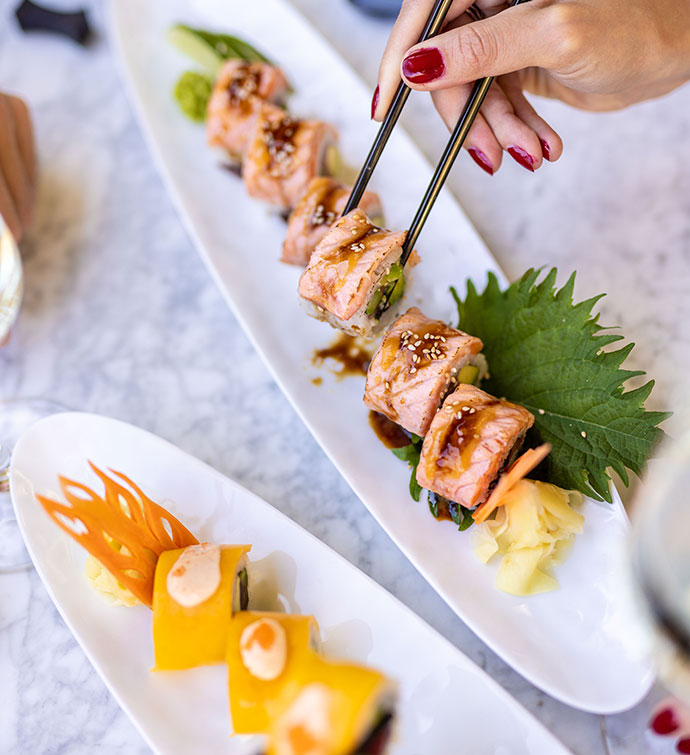 Deux plateaux de sushis de Mr Nakamoto - l'un garni de mangue, l'autre de saumon - avec 2 paires de mains ramassant un morceau avec des baguettes