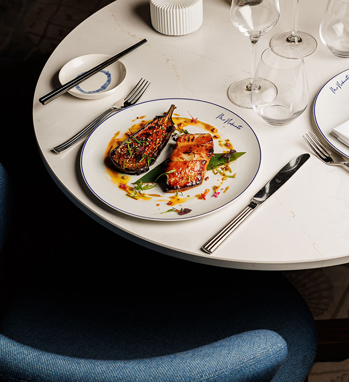 Un plato de bacalao negro del restaurante Mr. Nakamoto de Cannes, sobre una mesa de comedor puesta delante de una silla azul