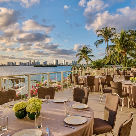 Outdoor dining table on a deck with ocean in the background and palm trees