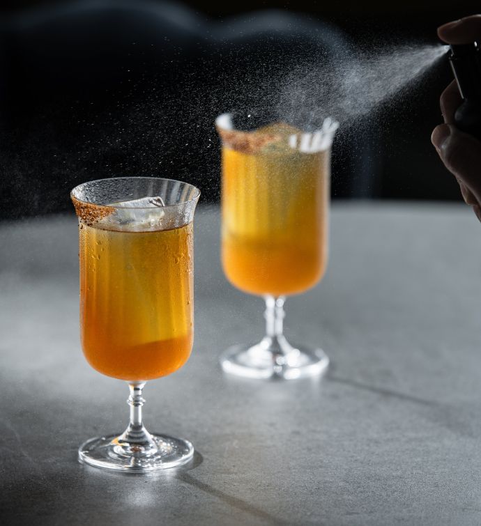 Two tall cocktails being sprayed with a garnish