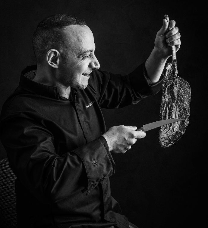 Black and white photo of a chef holding a steak and knife