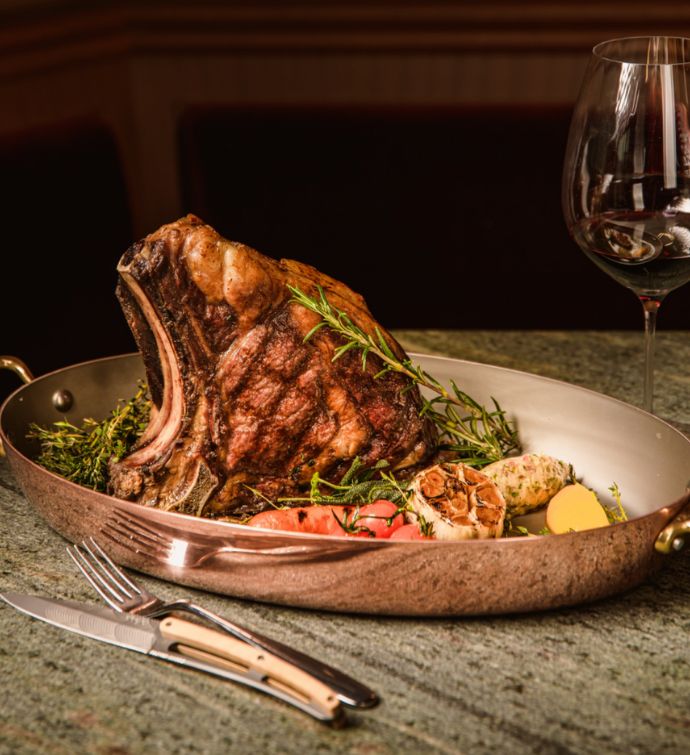 Steak with garnish in a copper pan accompanied by a red glass of wine