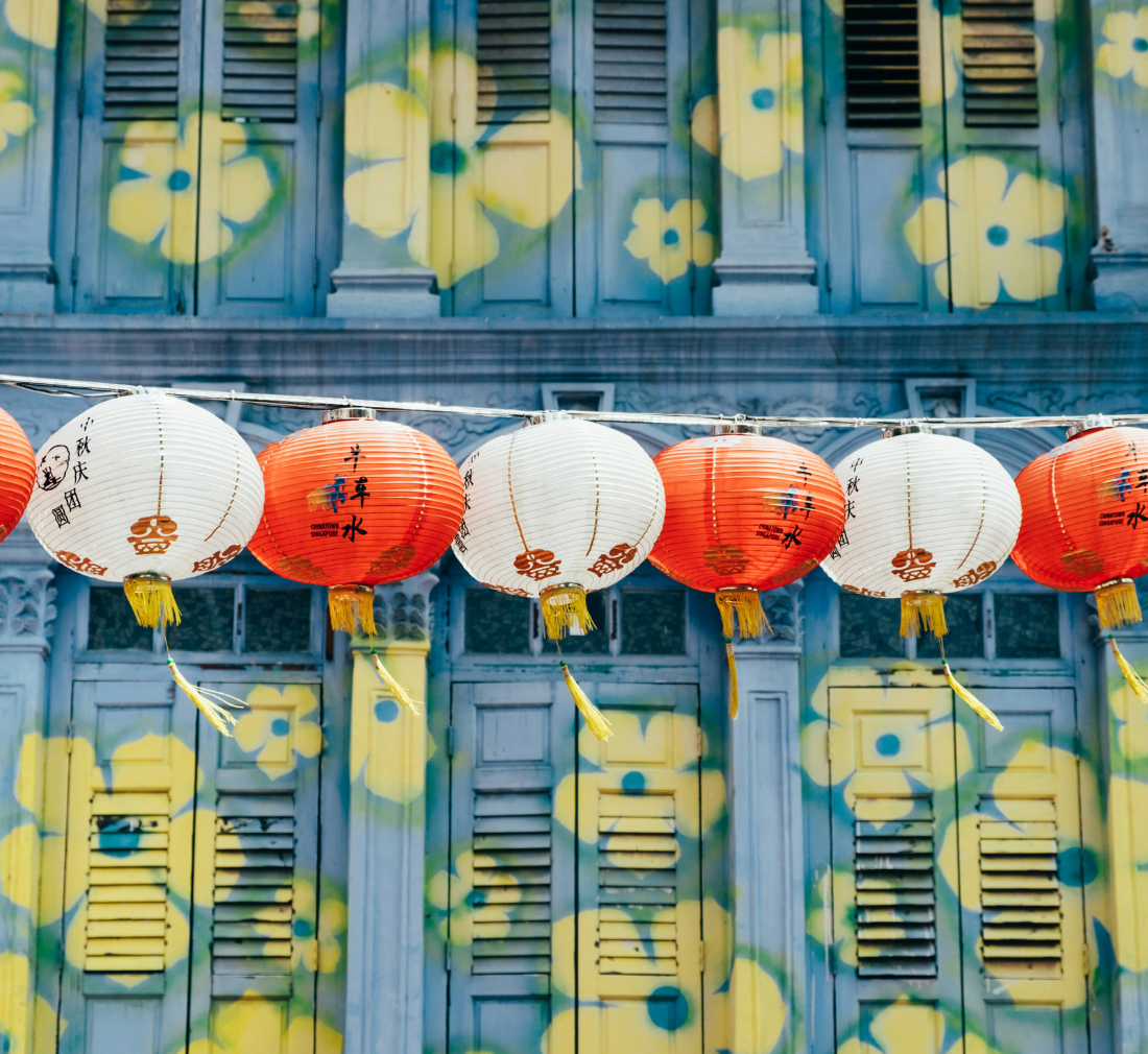 blue shophouse with yellow flowers painted on it, with chinese lanterns hanging above