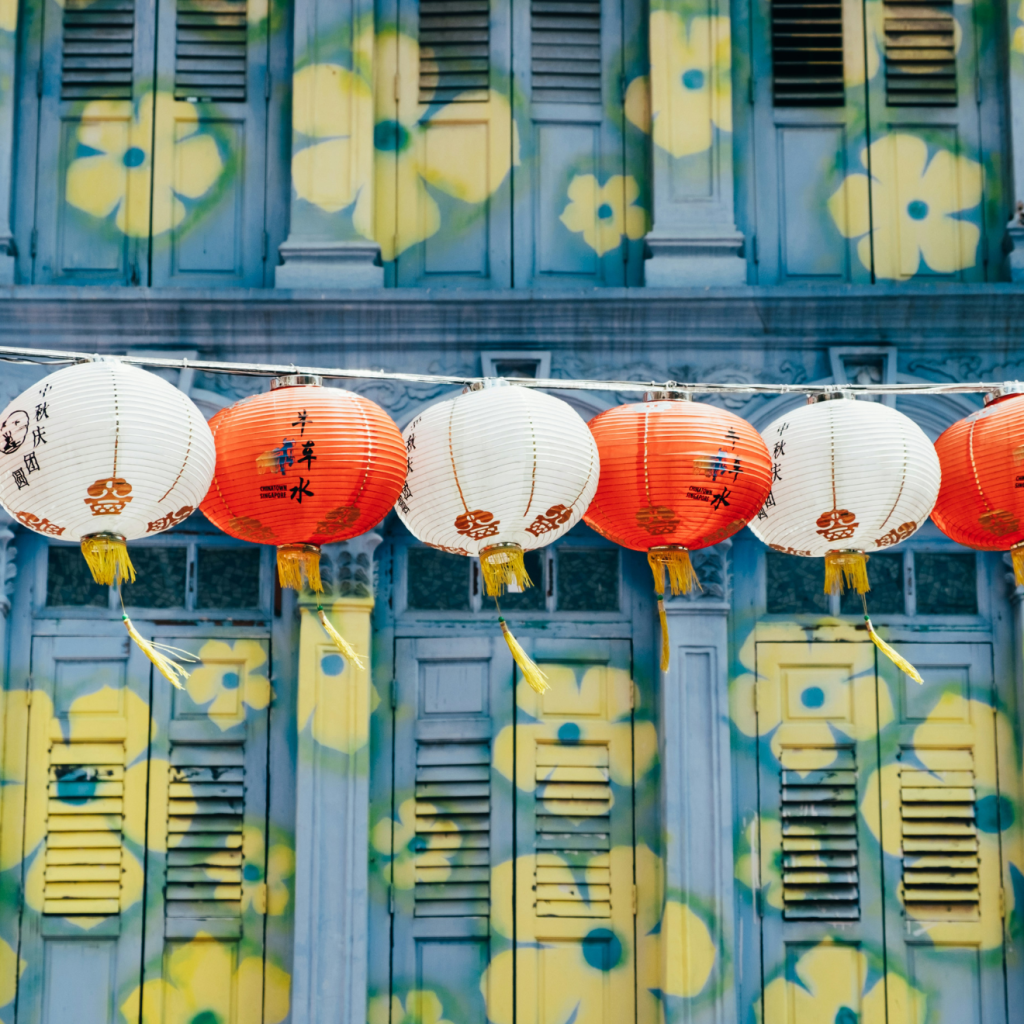 blue shophouse with yellow flowers painted on it, with chinese lanterns hanging above