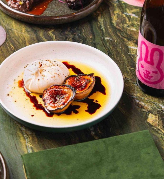 Burrata with fig, olive oil and balsamic on a plate accompanied by a bottle of wine