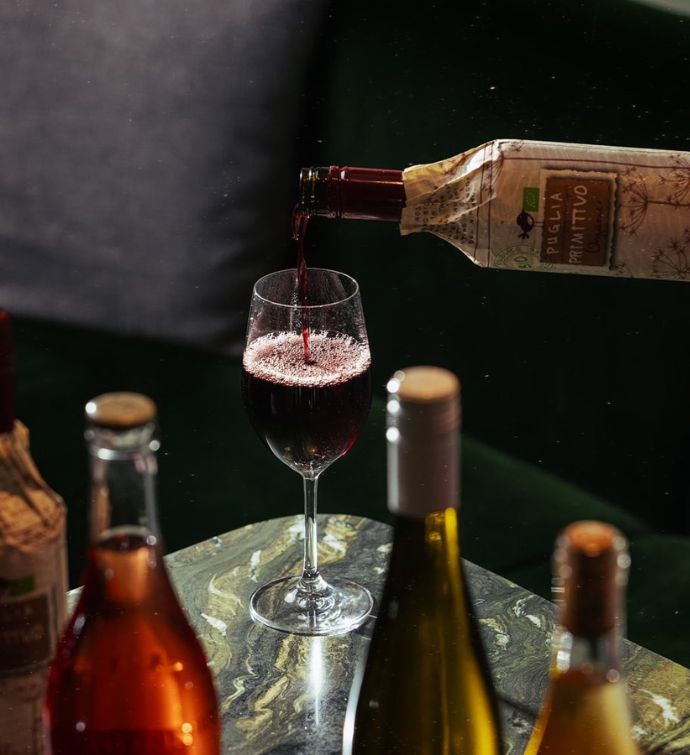 Bottle of red wine being poured surrounded by other bottles of wine