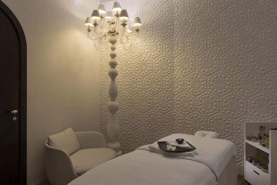 Massage treatment room at ESPA Doha with white walls, a massage bed and tall lamp