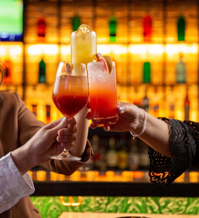 Three hands doing cheers at the Hudson Tavern bar with three cocktails