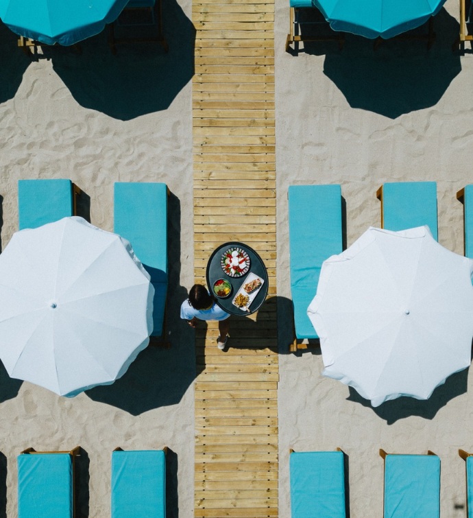 photo aérienne d'un serveur marchant sur la plage avec des chaises longues turquoise et des parasols blancs