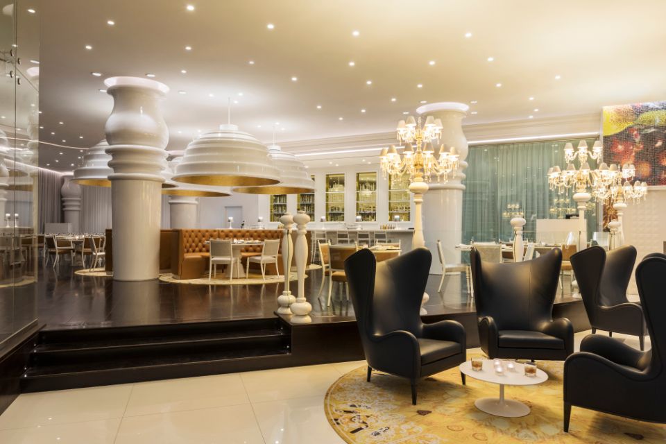 Interior of Mondrian Bistro with black chairs, a yellow rug and chandeliers