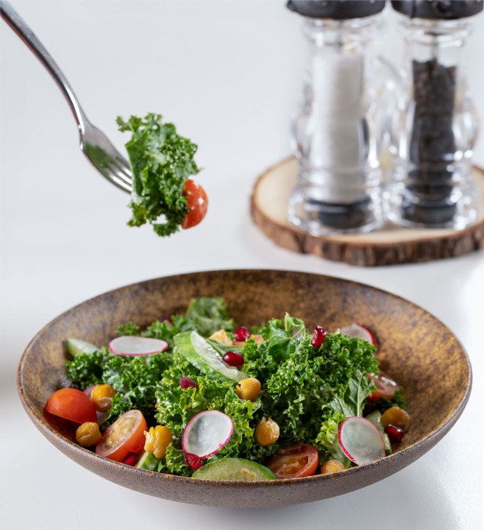 Fork lifting part of a kale salad with salt and pepper shakers in the background