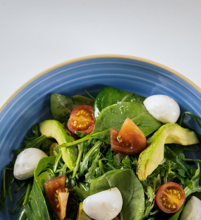 Fresh salad with avocado, mozzarella and tomato in a blue bowl