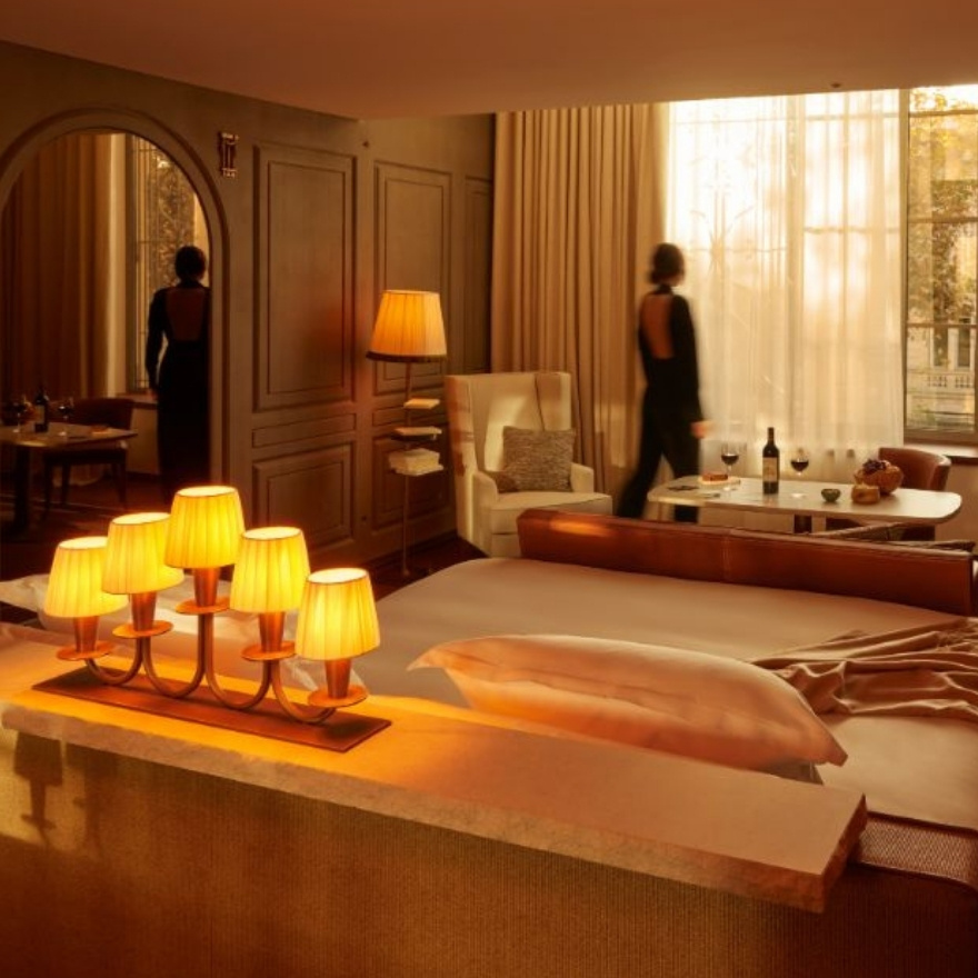 Warmly lit bedroom with woman in black walking to the window