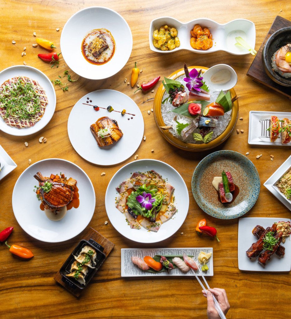 Plusieurs plats japonais sur des assiettes de formes et de couleurs différentes reposent sur une table en bois clair