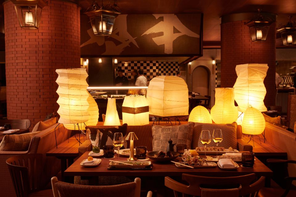 Warmly lit restaurant with paper lamps on a rectangle wooden table with dinner set and stemware