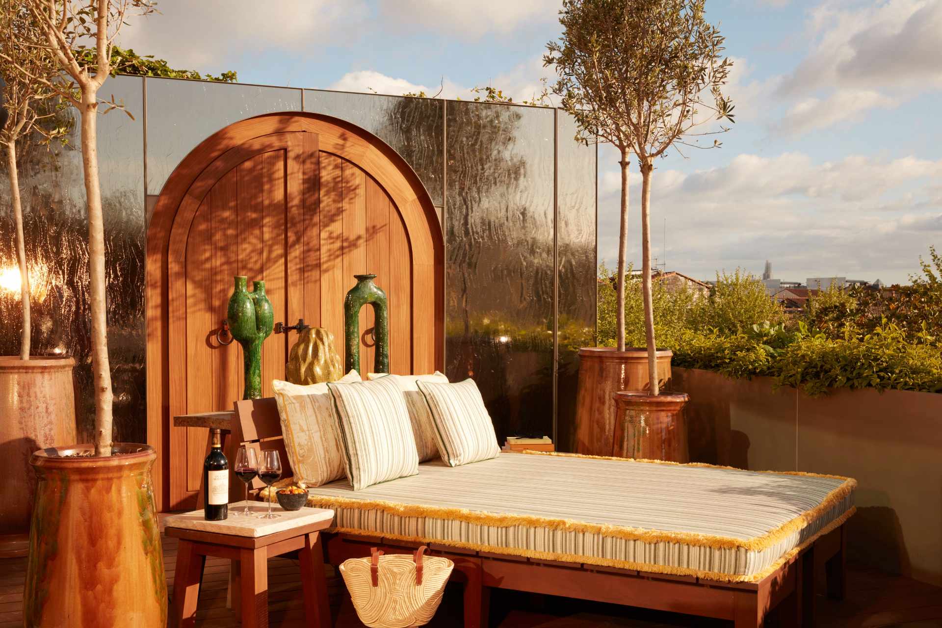 A daybed on a patio accompanied by a table, trees and a purse.