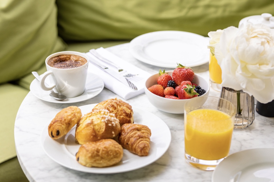 Table garnie avec un petit déjeuner comprenant du café, du jus de fruits, des viennoiseries et des fraises