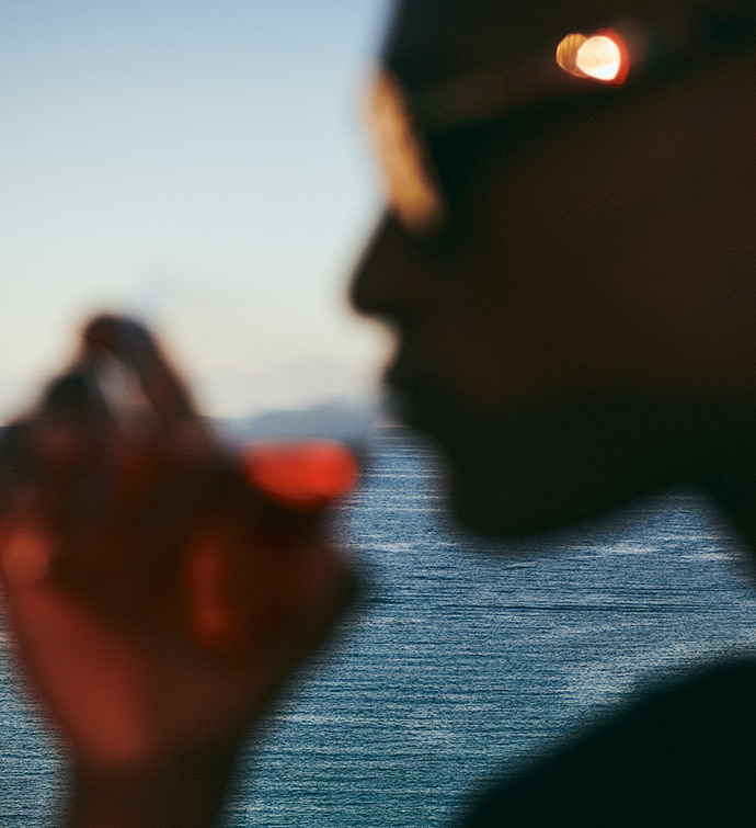 Image en gros plan d'une personne portant un cocktail à sa bouche avec la mer en arrière-plan