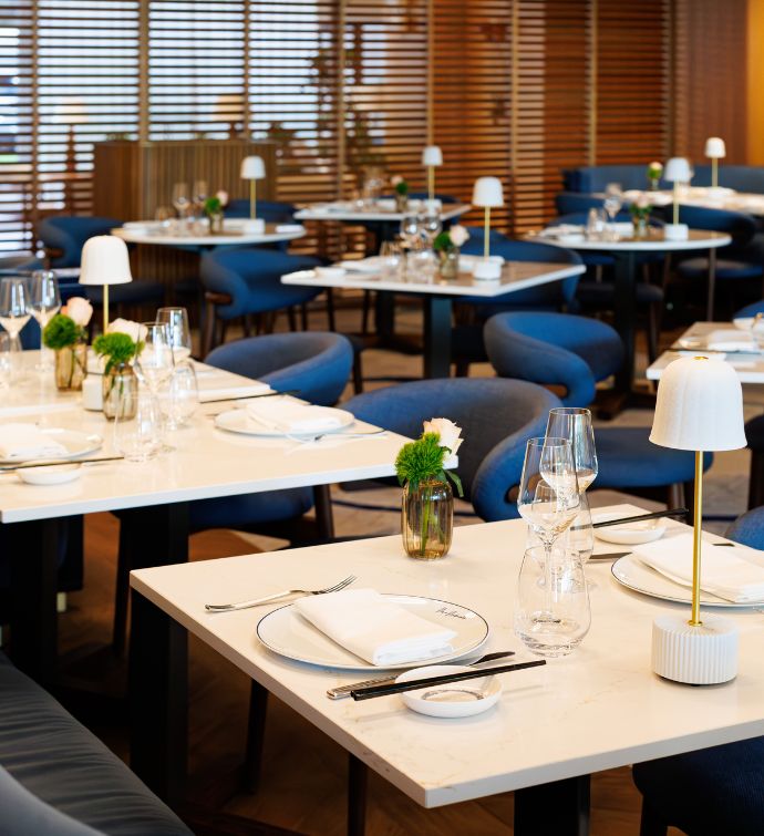 Fila de mesas de comedor blancas cuadradas con cubiertos y lámpara pequeña con sillas de comedor azul marino