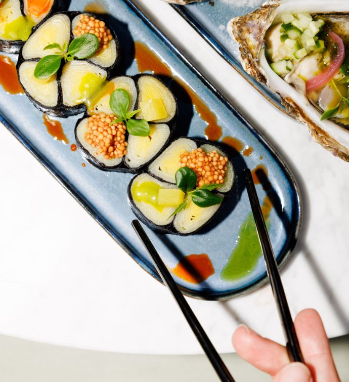 Longue assiette ovale bleue avec des rouleaux de sushi et des doigts tenant une baguette hors du cadre