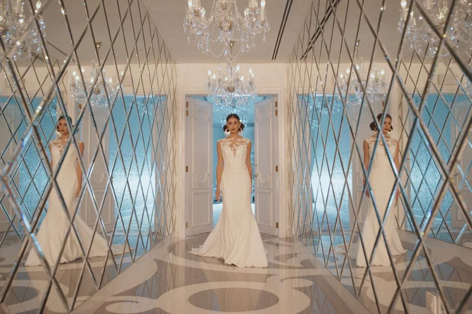 Woman in a wedding dress walking down a hallway with mirrors and a chandelier