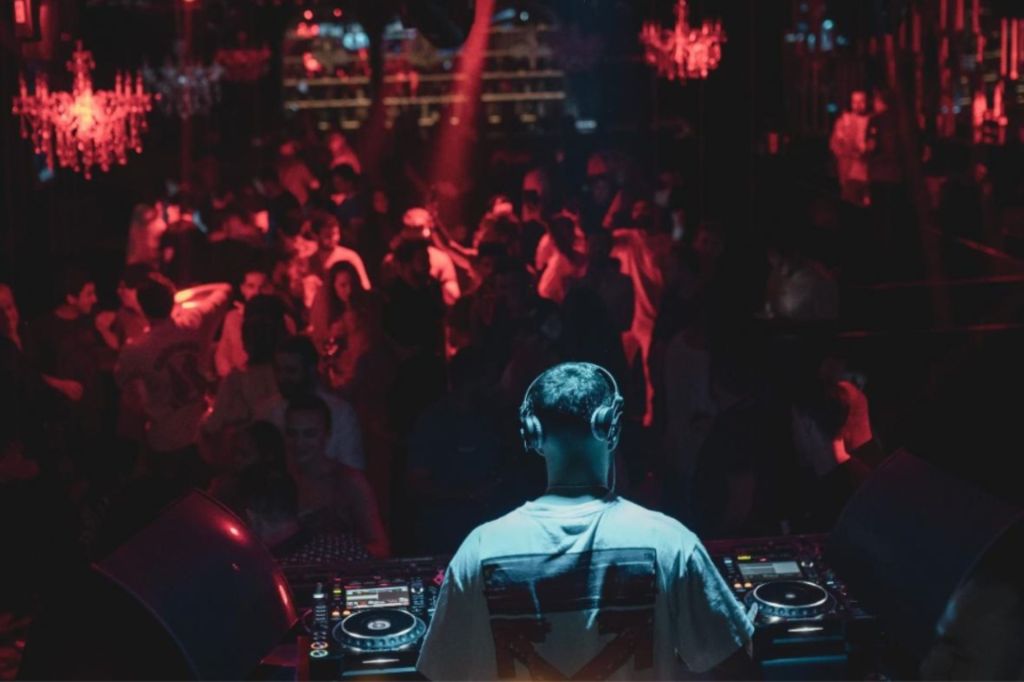 un club lleno de luces rojas desde la perspectiva del dj, con luz brillando sobre él