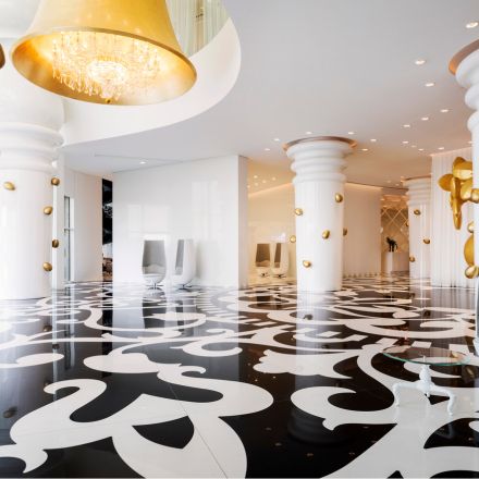 Large lobby with black and white intricate tile, large white columns, and gold wall decorations