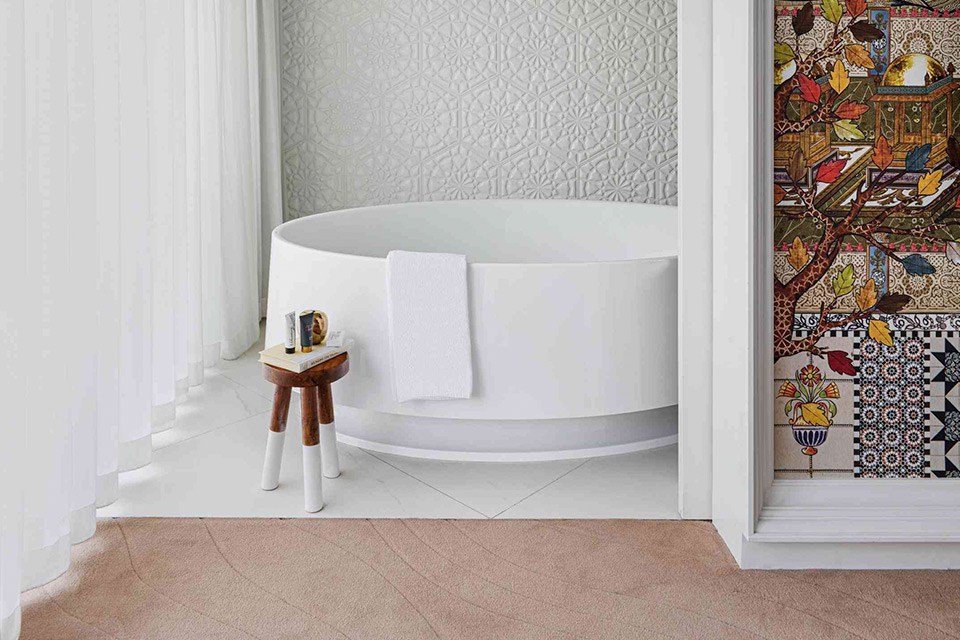 A bathroom with a white tub and a wall adorned with vibrant tiles.