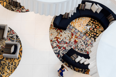 Aerial view of a lobby with white tile floors, decorative rugs, and black curved sofas