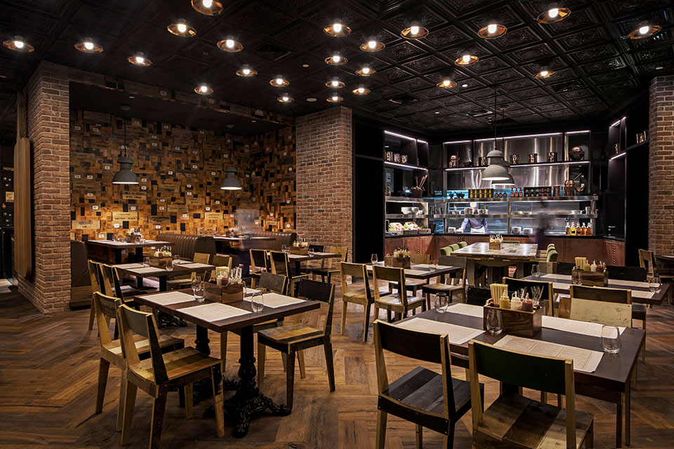 Dining room with brown wooden floors, brick wall, and small square four top tables throughout.