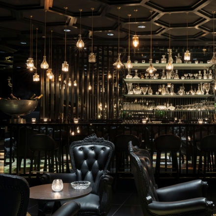 Smoke & Mirrors Doha interior with black leather chairs, hanging lights and a bar