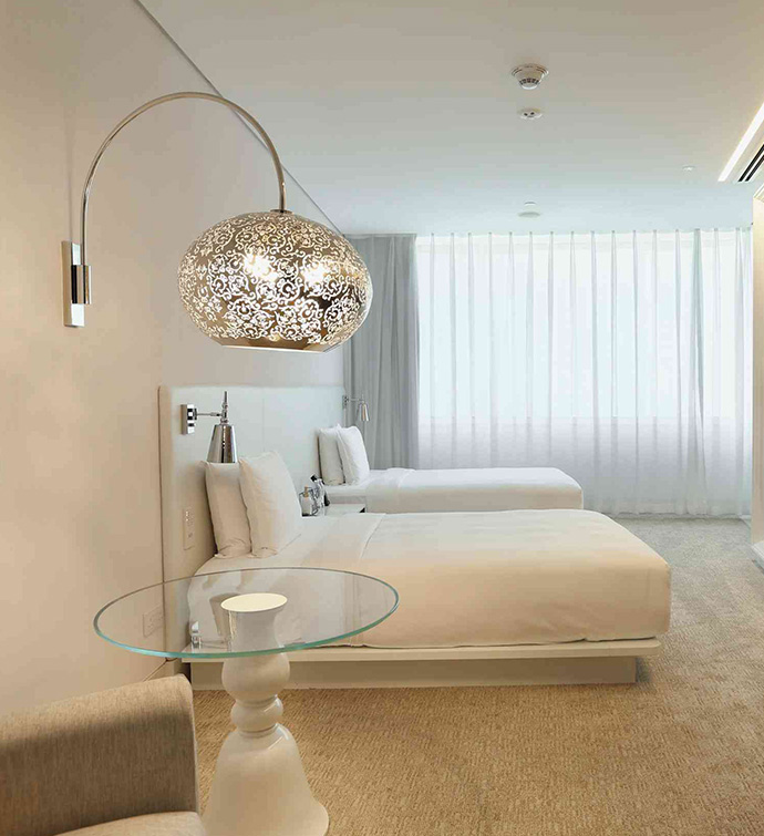 A bedroom with two beds and a large silver wall lamp.