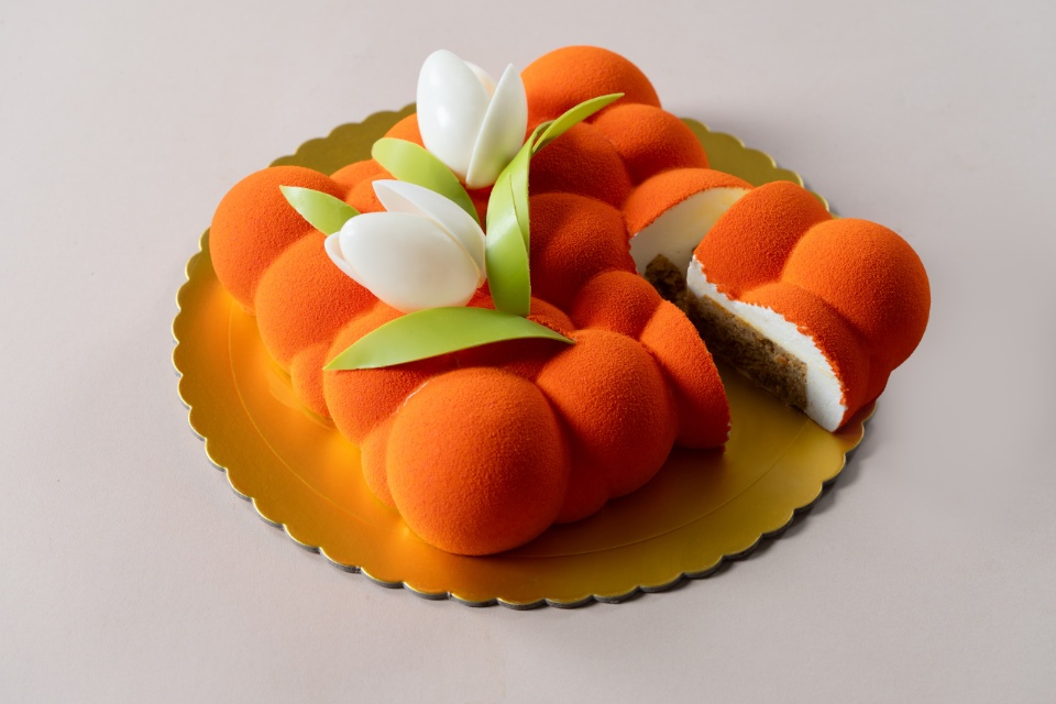 Image of an artistic orange dessert slightly cut open with flowers on top