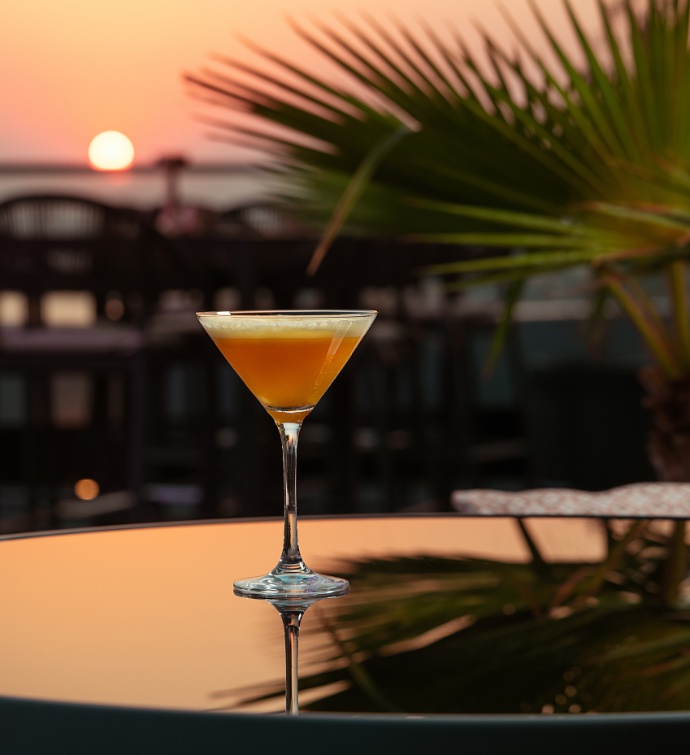 Orange cocktail in a martini glass on a table at sunset