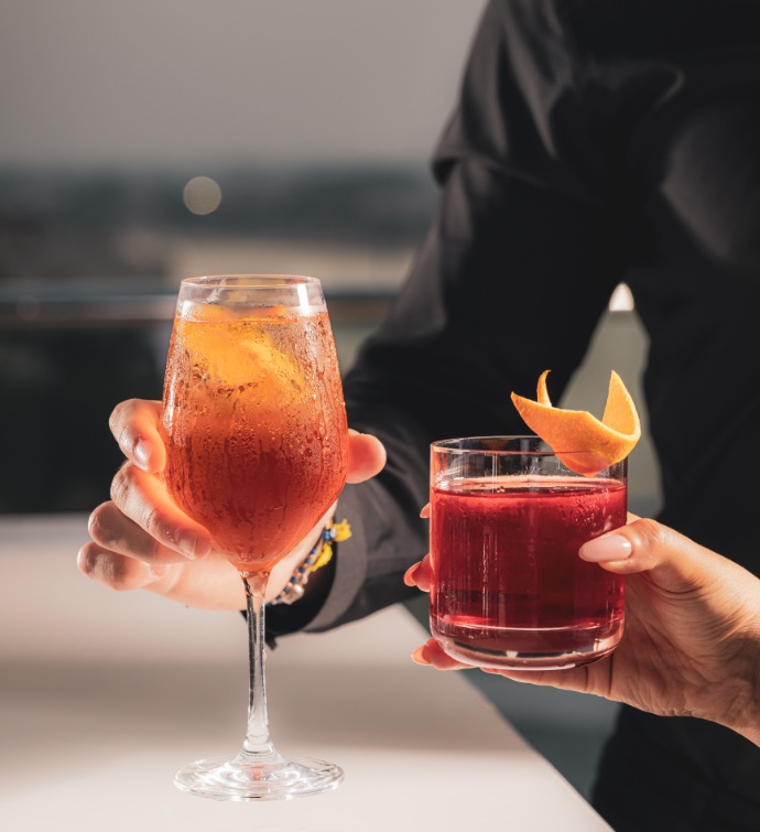 Two people holding an orange and red cocktail