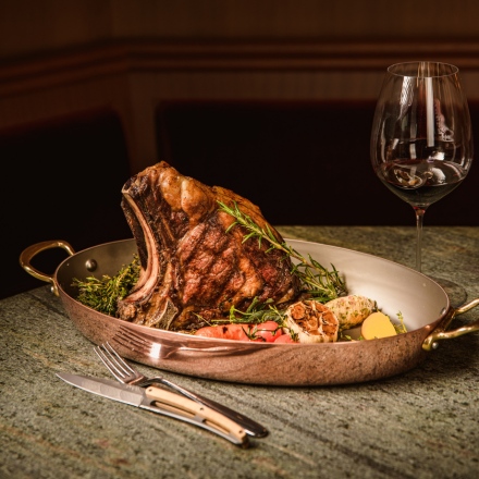 Steak with garnish in a copper pan accompanied by a red glass of wine