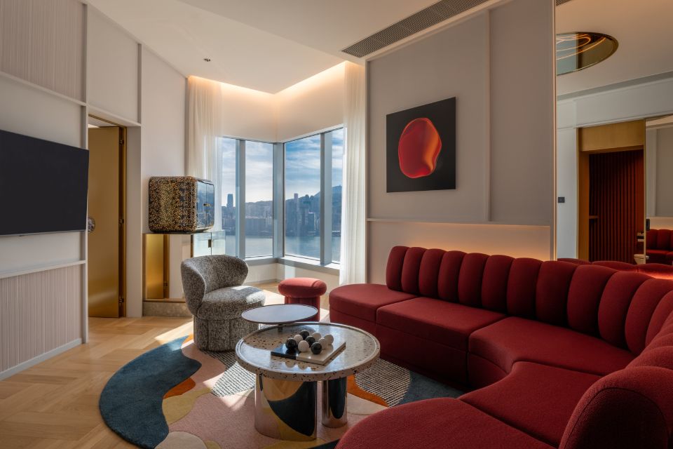 Hotel room with large semi-circle couch, table, tv and view of the harbour